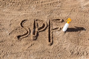 Sun protect factor. SPF word written on the sand and white bottle with suntan cream. Skin care concept background