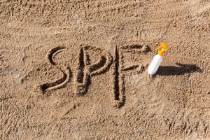Sun protect factor. SPF word written on the sand and white bottle with suntan cream. Skin care concept background Sun protect factor. SPF word written on the sand and white bottle with suntan cream. Skin care concept background